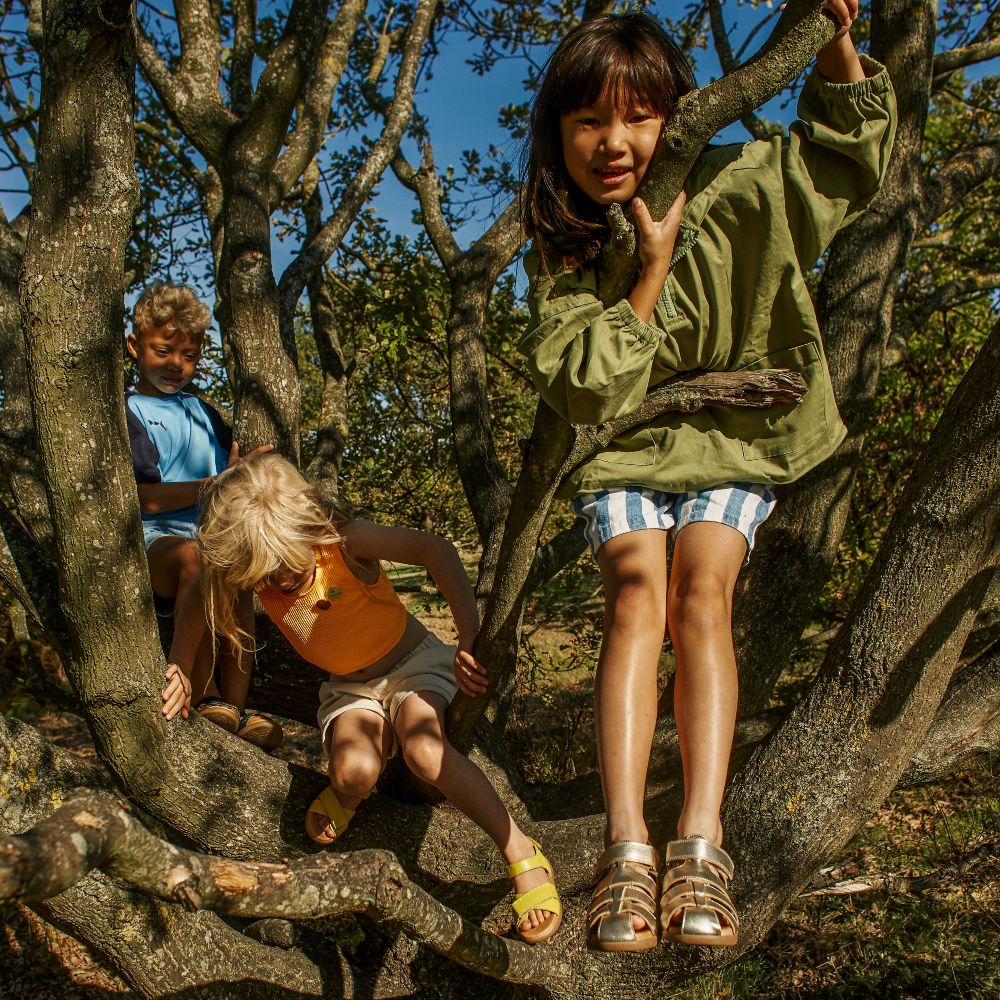 Children climbing in a tree wearing sandals by Zig + Star 