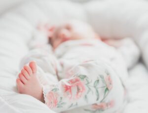 Newborn baby lying on white bedding wearing white and pink floral trousers