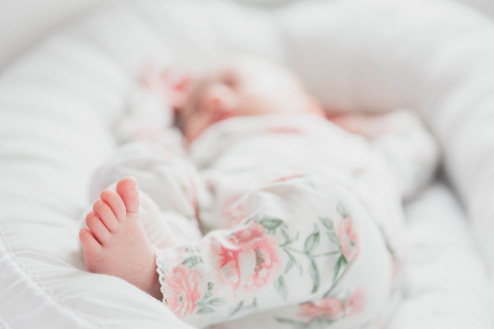 Newborn baby lying on white bedding wearing white and pink floral trousers