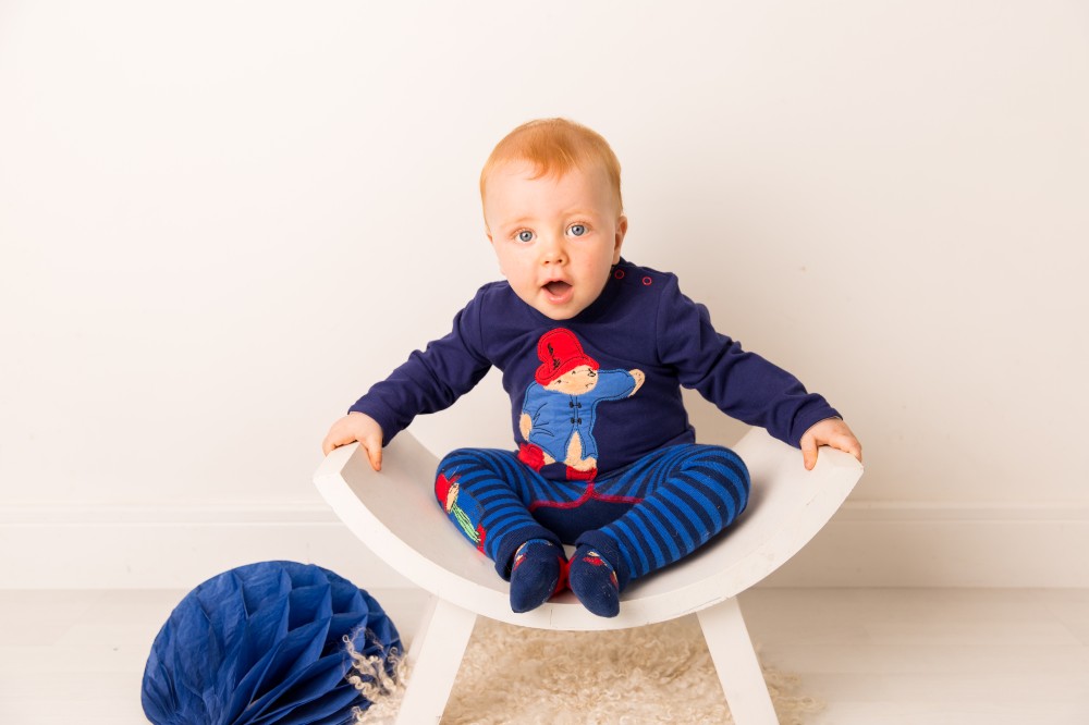 A baby sat in a white chair wearing a Paddington™ Bear top, leggings and socks by Blade & Rose
