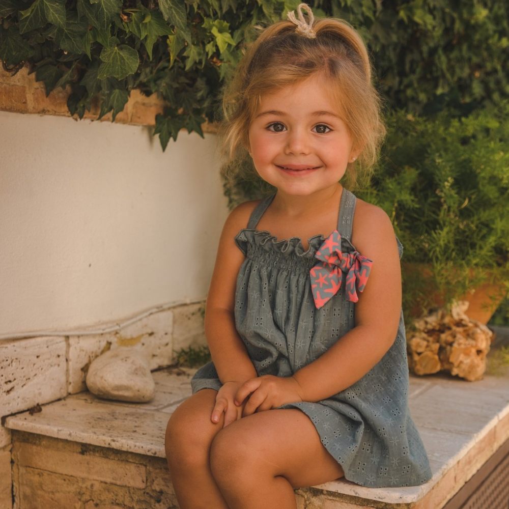 Young girl sat on a wall wearing a grey dress with a pink bow 