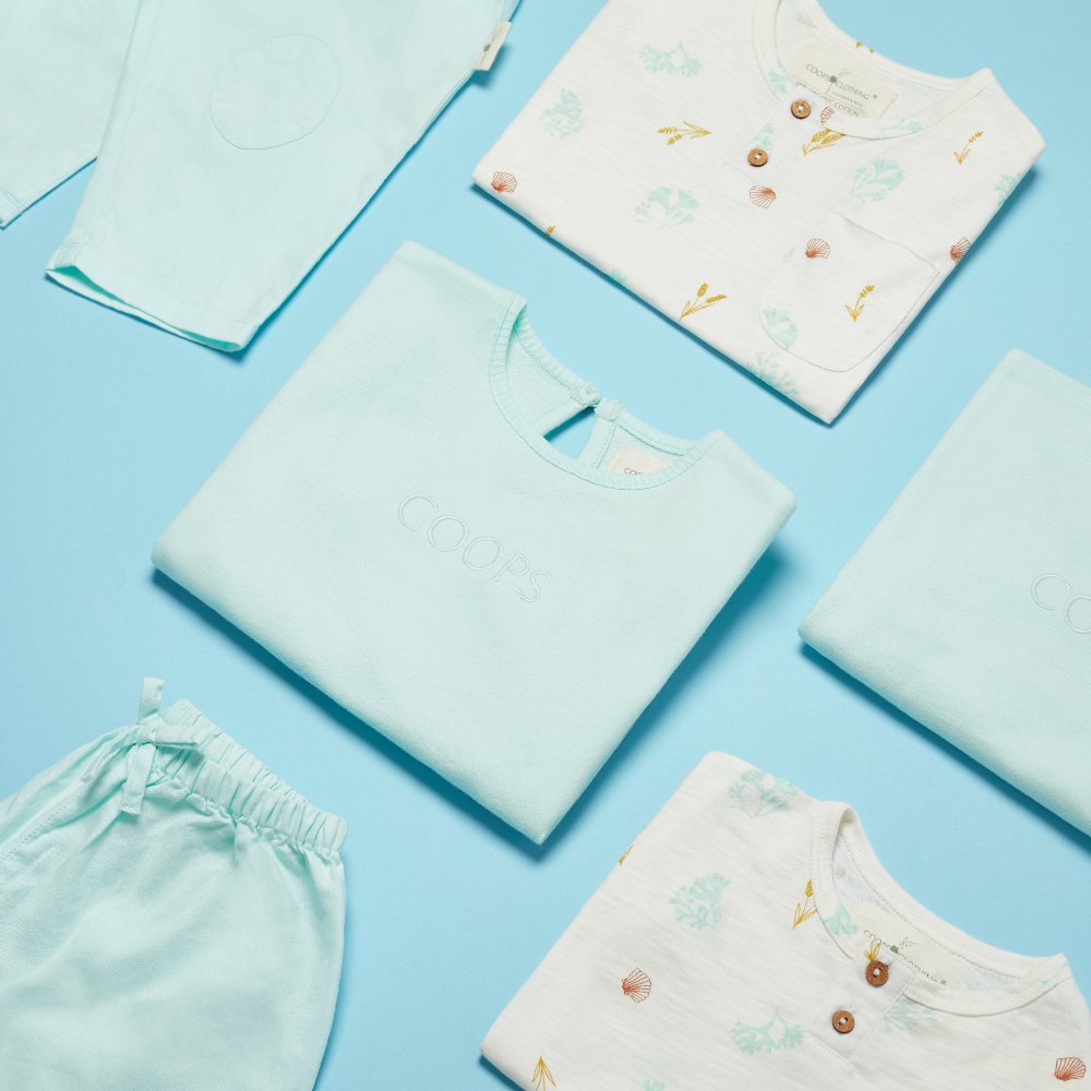 A display of blue and white baby clothing by Coops Clothing on a blue background