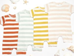 Four striped baby rompers displayed on the floor with seashells