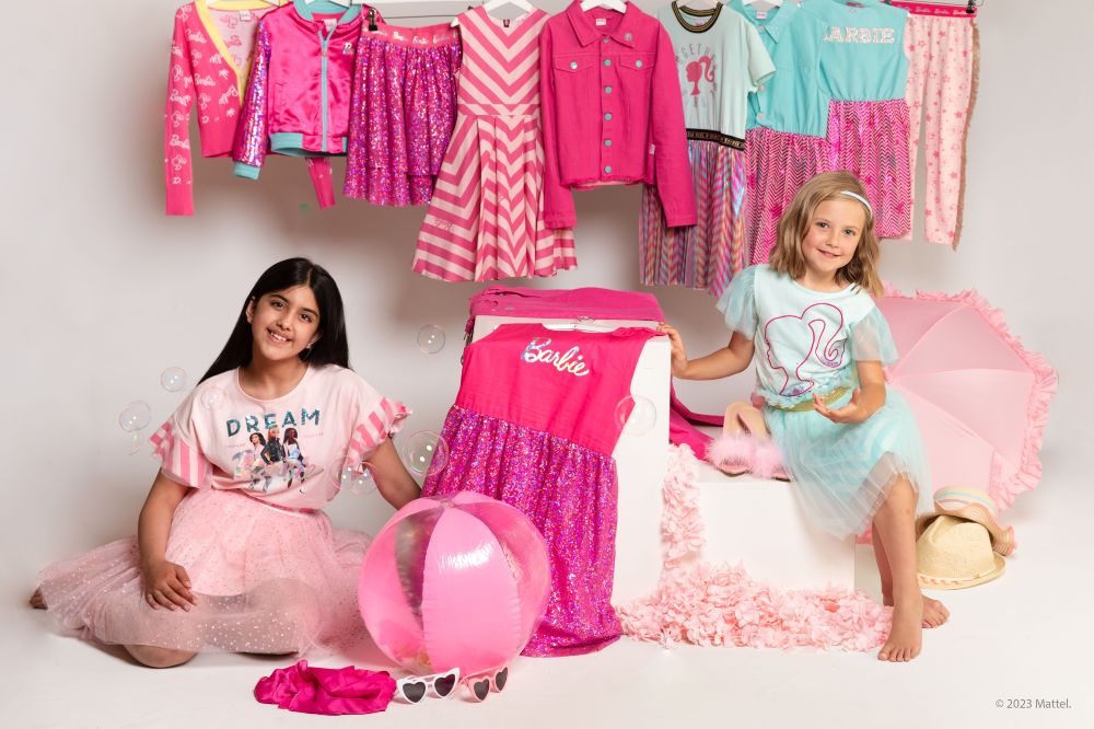 Two girls sat down surrounded by pink Barbie clothing by Erve