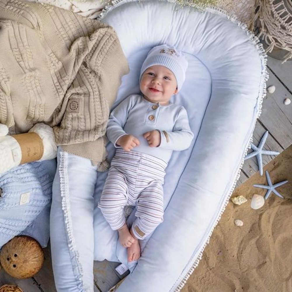 A young baby dressed in blue lying on a pillow on the floor 