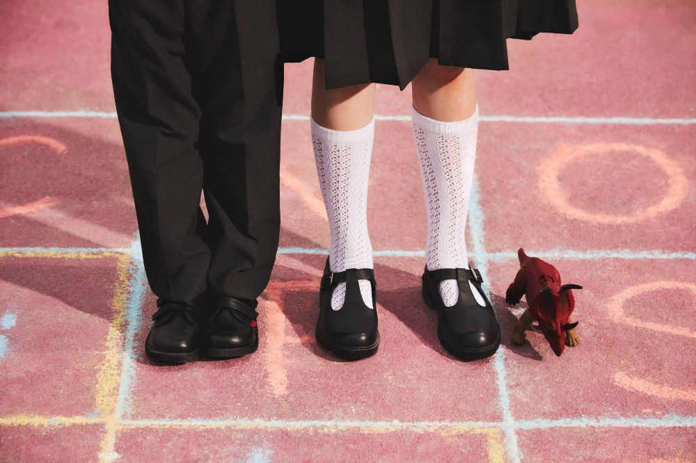 Two children's legs stood on a pink floor wearing school shoes 