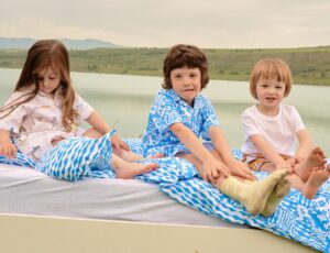 Three children sat outside on a bed with blue bedding