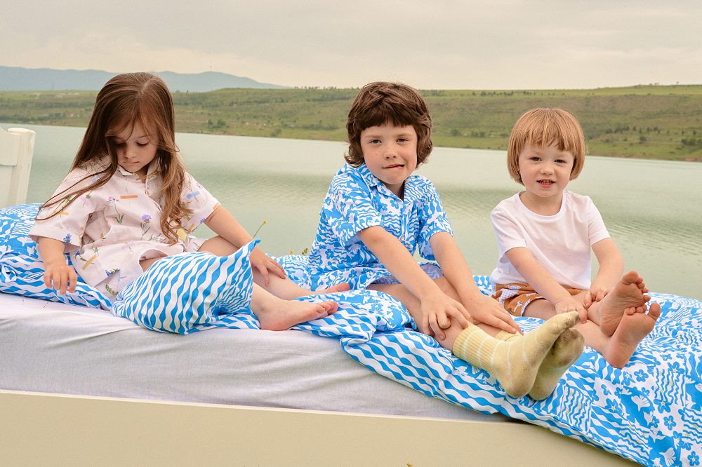 Three children sat outside on a bed with blue bedding
