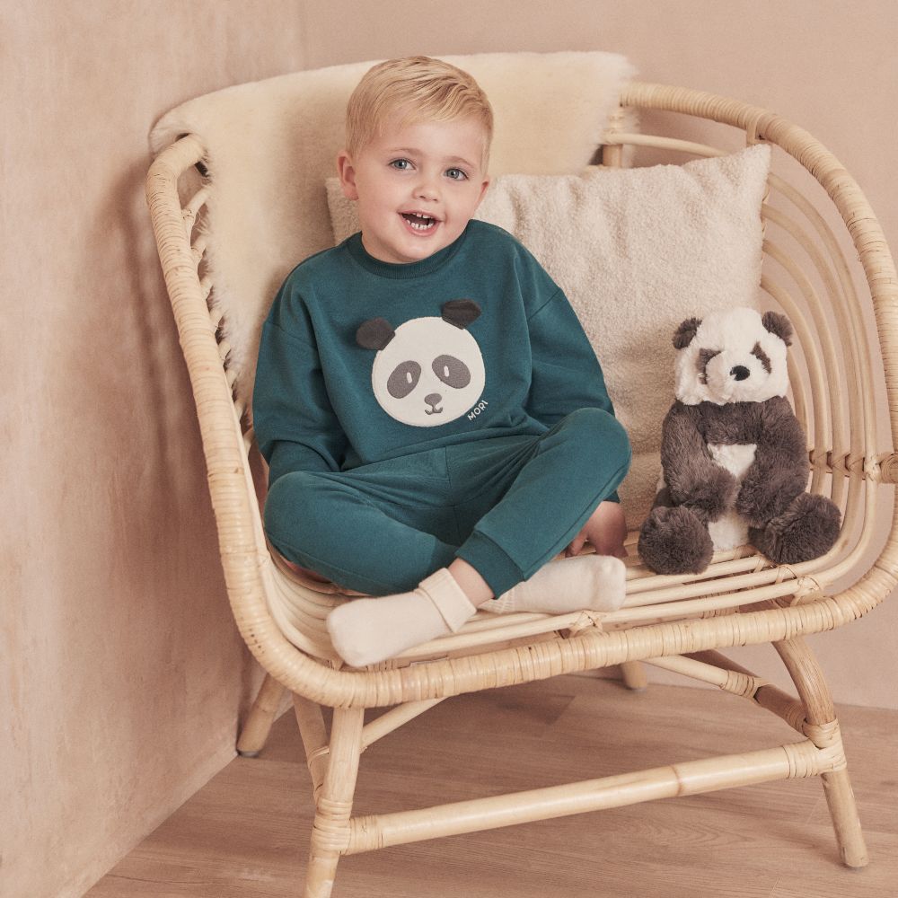A young boy sat in a chair beside a toy panda wearing a top with a panda face on the front