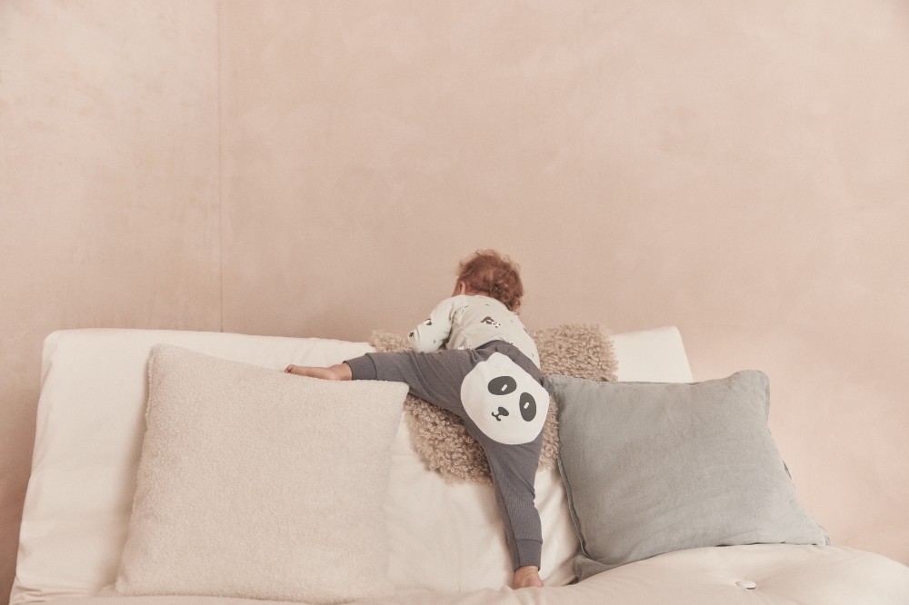 The back of a young child climbing on a sofa wearing leggings with a panda face on the bottom