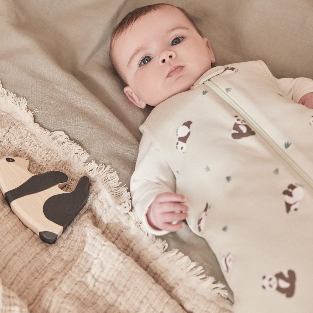 A baby lying down wearing a panda print sleepsuit by MORI