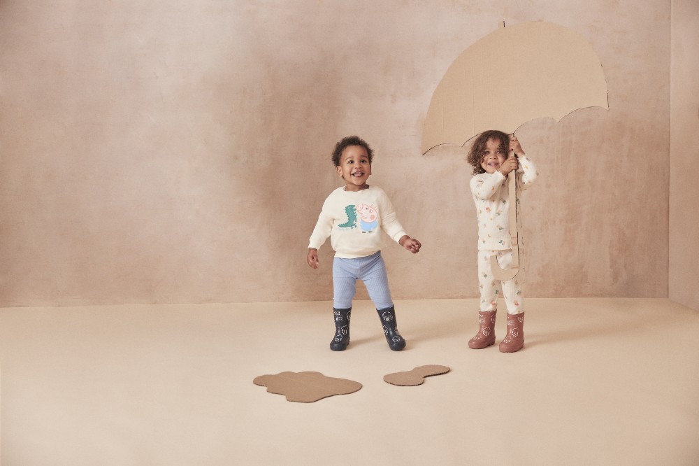Two children with a cardboard umbrella wearing the Peppa Pig by Mori childrenswear collection