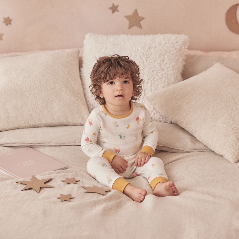 A young child sat on a bed surrounded by cardboard stars wearing pyjamas from the Peppa Pig by Mori collection 