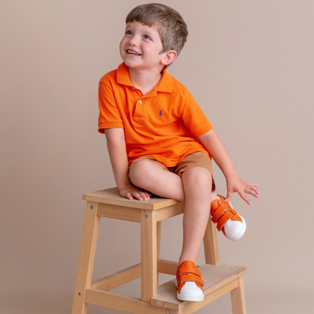 Young boy sat on a stool wearing an orange T-shirt and orange trainers 