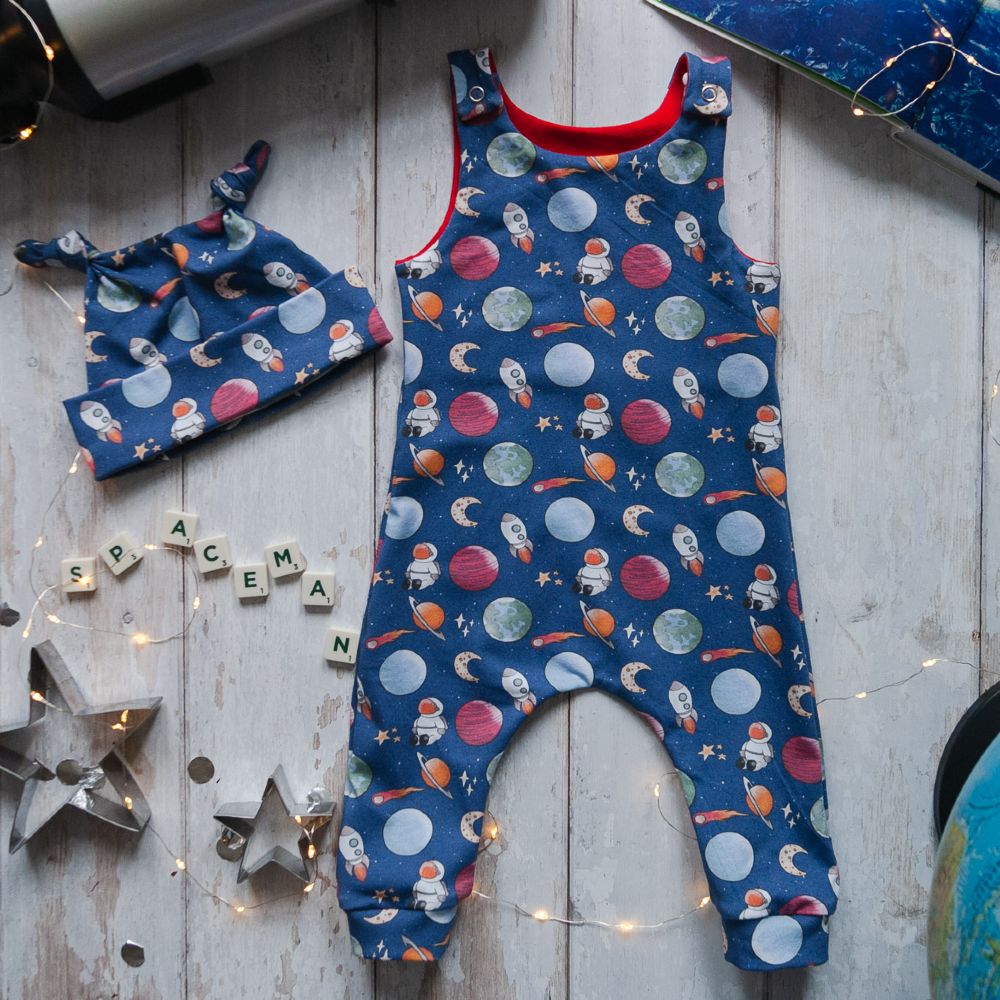 A space print baby romper and hat by Taffy Tots Clothing displayed on the floor