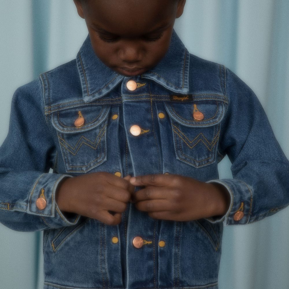 Young boy looking down buttoning up a blue denim jacket 