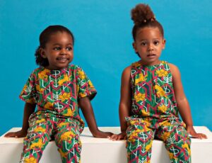 Two children sat on a white seat wearing colourful outfits by Akwa Baby