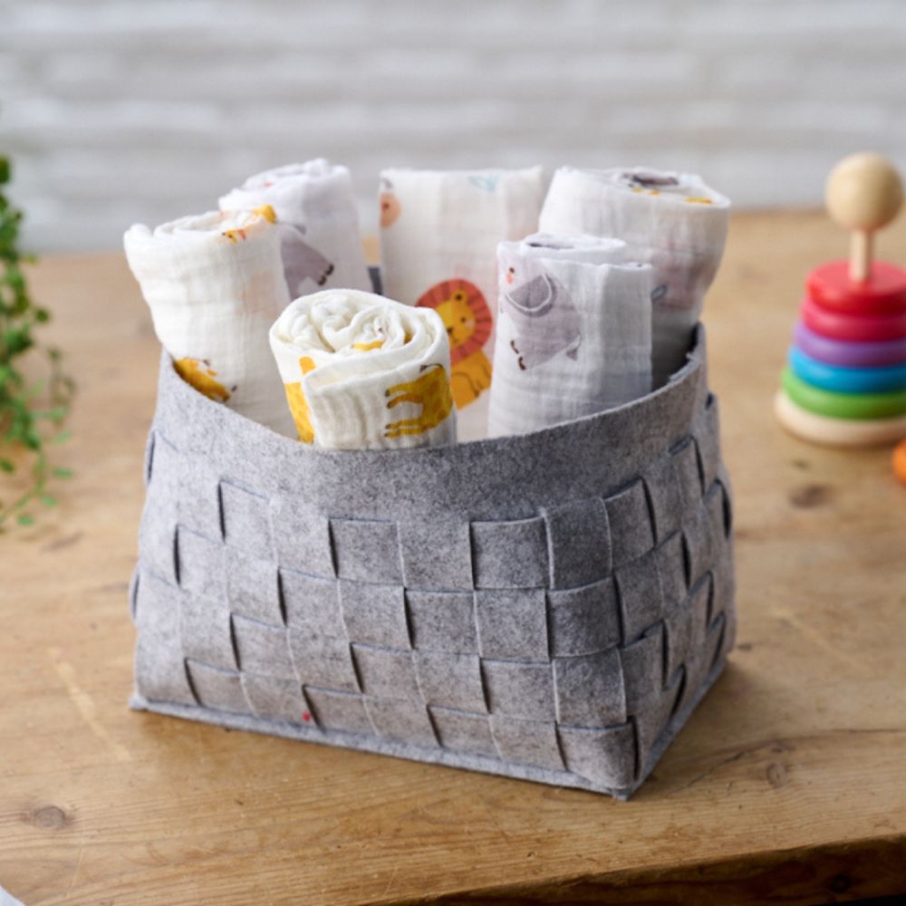 A grey storage basket containing baby muslins with animals printed on them