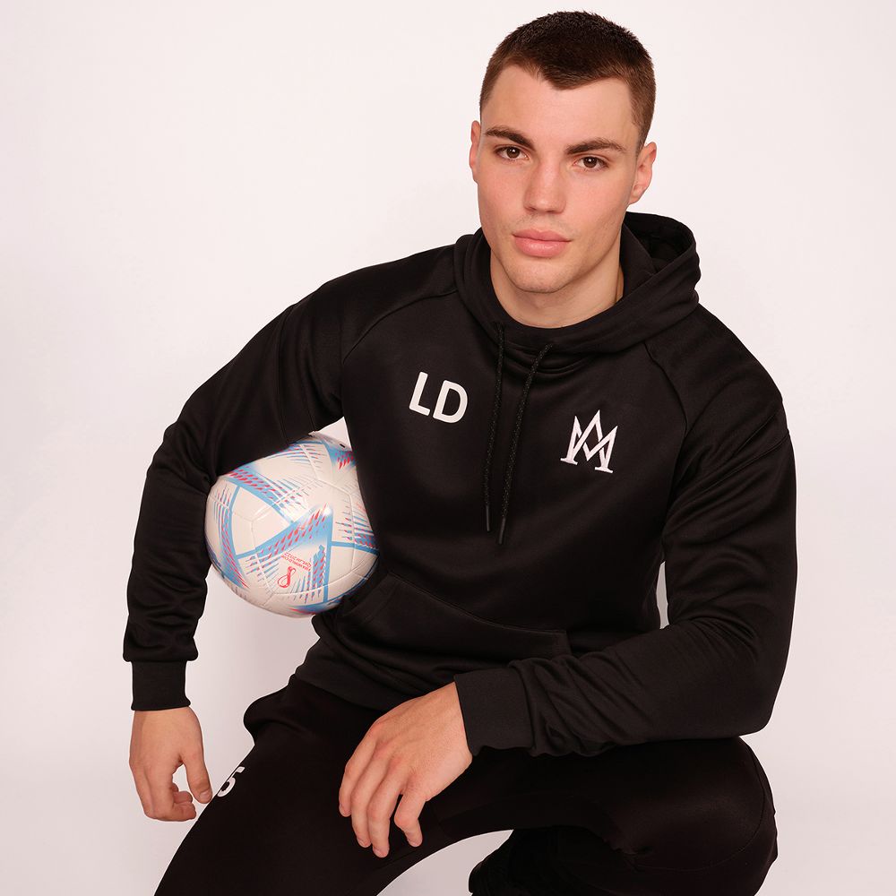 A man knelt down wearing a black tracksuit holding a ball 