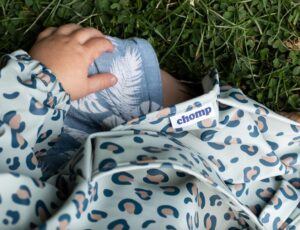 A baby sat on the grass wearing an animal print bib by Chomp