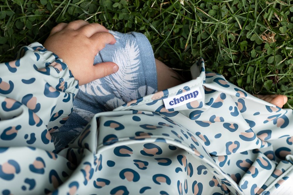 A baby sat on the grass wearing an animal print bib by Chomp