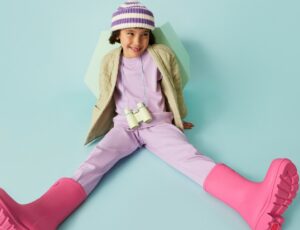 A young girl sat on a blue floor wearing pink Wellington boots by FitFlop