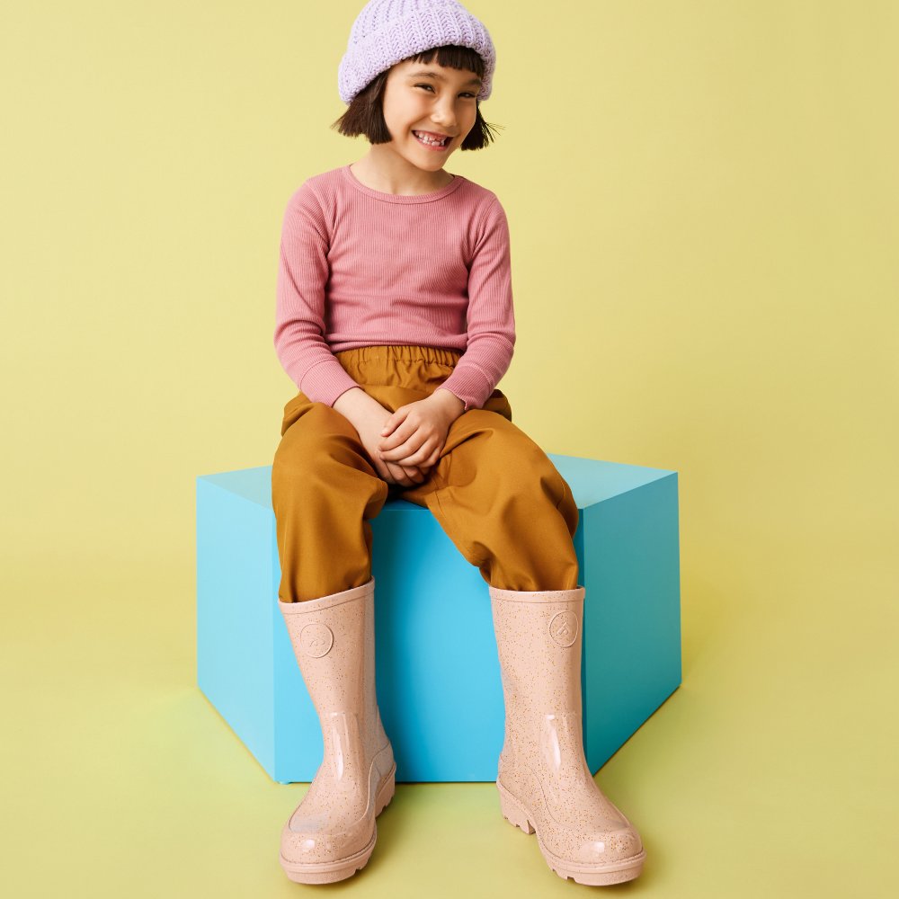 A young girl sat on a blue box wearing pink Wellington boots by FitFlop