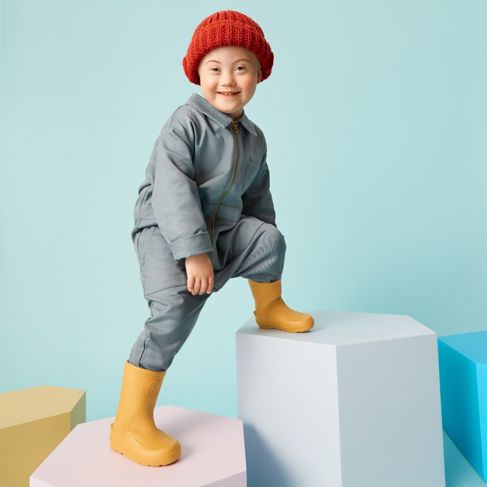 A young boy climbing on white cubes wearing yellow Wellington boots by FitFlop