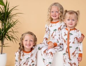 Three children sat together wearing giraffe print sleepwear by GrowGrows