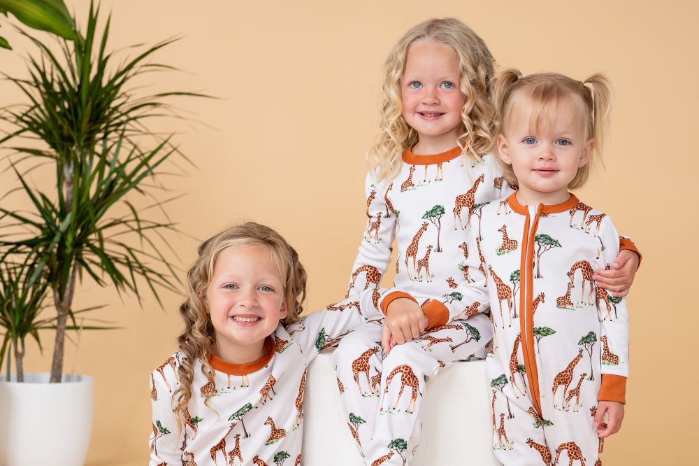 Three children sat together wearing giraffe print sleepwear by GrowGrows