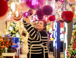 A woman stood on a step ladder in a shop hanging Christmas baubles