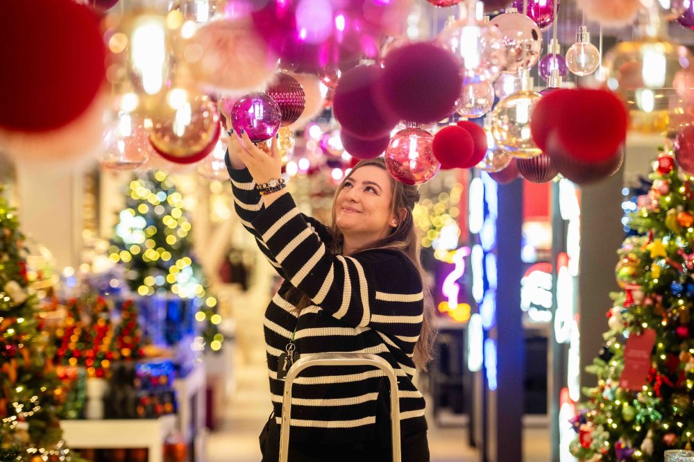 A woman stood on a step ladder in a shop hanging Christmas baubles