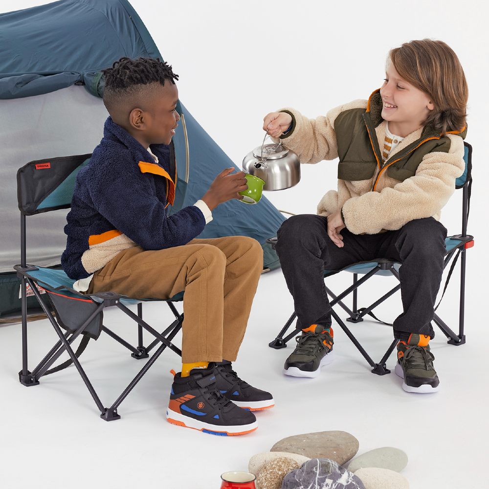 Two young boys sat in camping chairs beside a tent 