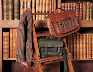 Two satchel's sat on a wooden step ladder next to a bookshelf