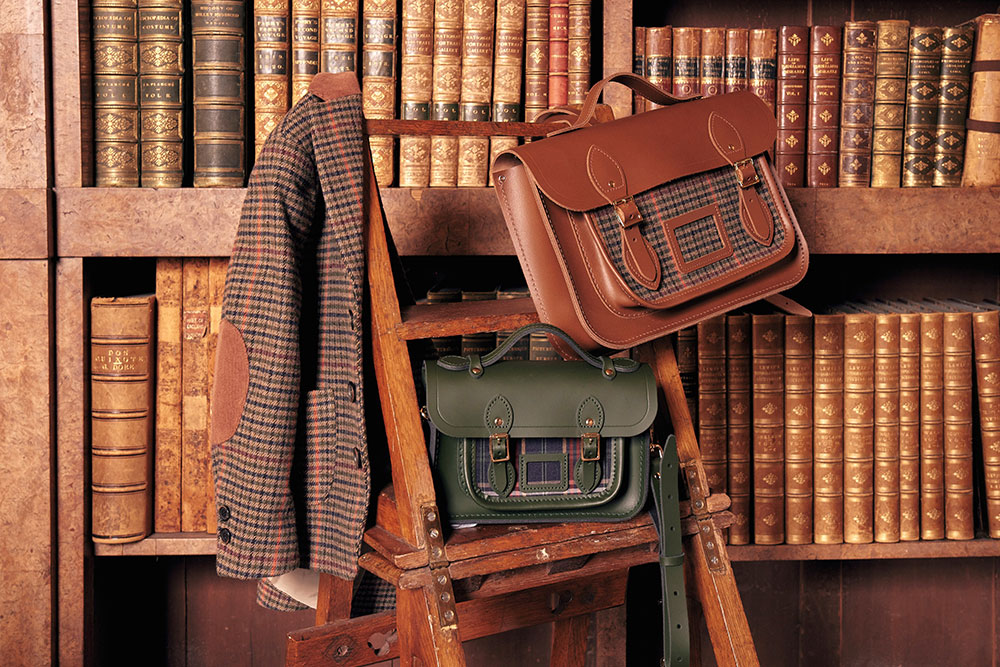 Two satchel's sat on a wooden step ladder next to a bookshelf