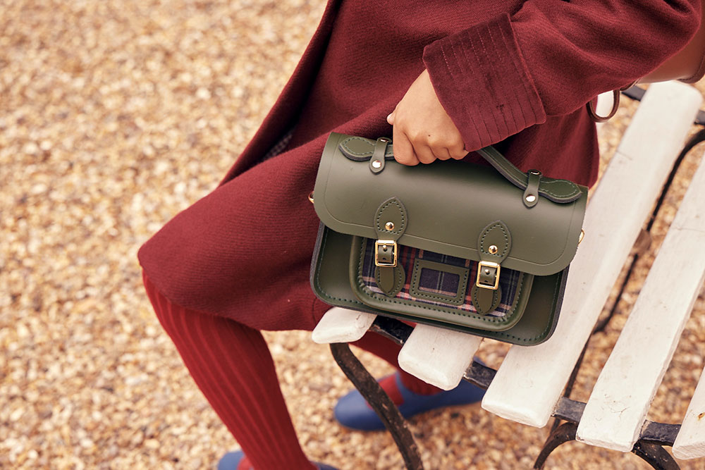 A girl in school uniform sat on a bench holding a racing green satchel