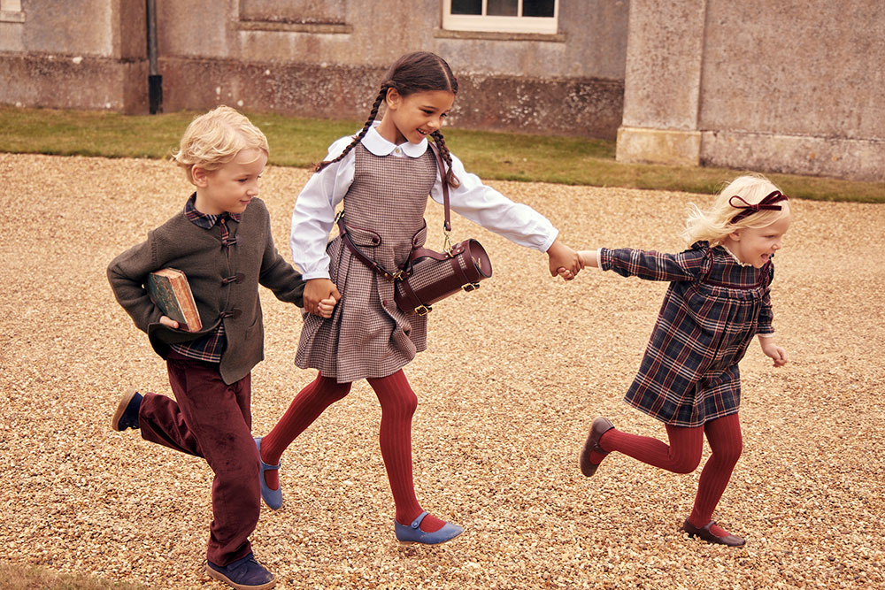 Two girls and a boy in school uniform running while holding hands