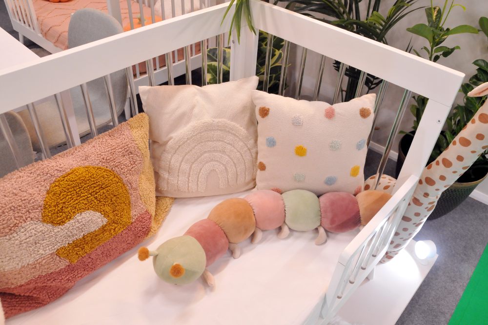 A baby's crib decorated with cushions and a caterpillar toy at Harrogate International Nursery Fair