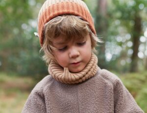 A boy stood in a wood wearing a hat and jumper by KIDLY