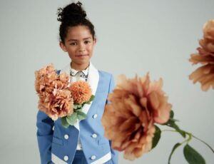 A young girl wearing a blue and white jacket beside pink flowers