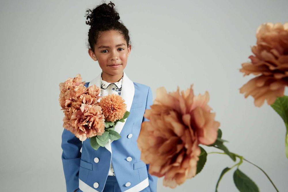 A young girl wearing a blue and white jacket beside pink flowers