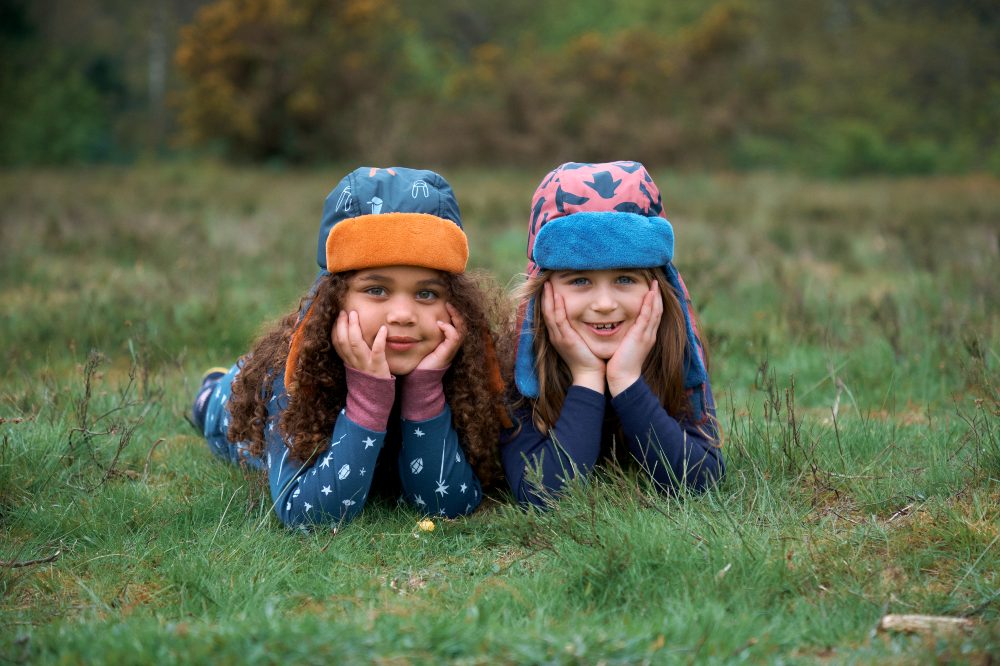 Two children lying on grass wearing deer hunter hats 