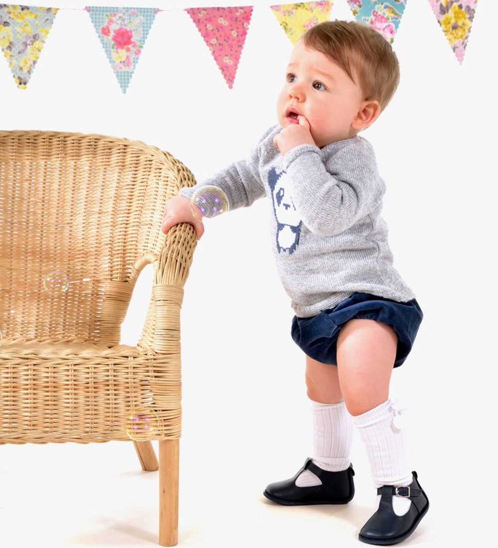 A young boy holding onto a chair wearing a jumper, shorts and knee socks by Pex