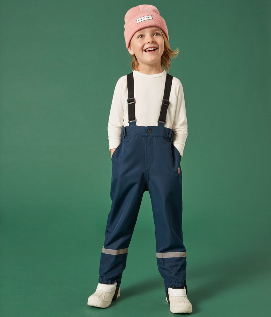 A young child wearing a pink hat, white top and blue waterproof trousers by Roarsome 