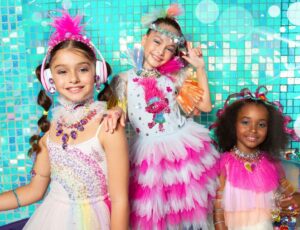 Three girls wearing brightly coloured dresses and hair accessories from the Tutu Du Monde x Trolls Band Together Collection