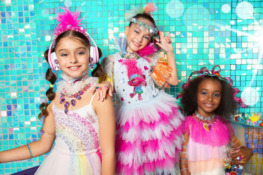 Three girls wearing brightly coloured dresses and hair accessories from the Tutu Du Monde x Trolls Band Together Collection