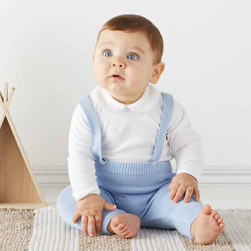 A baby sat on the floor wearing a white top and blue dungarees