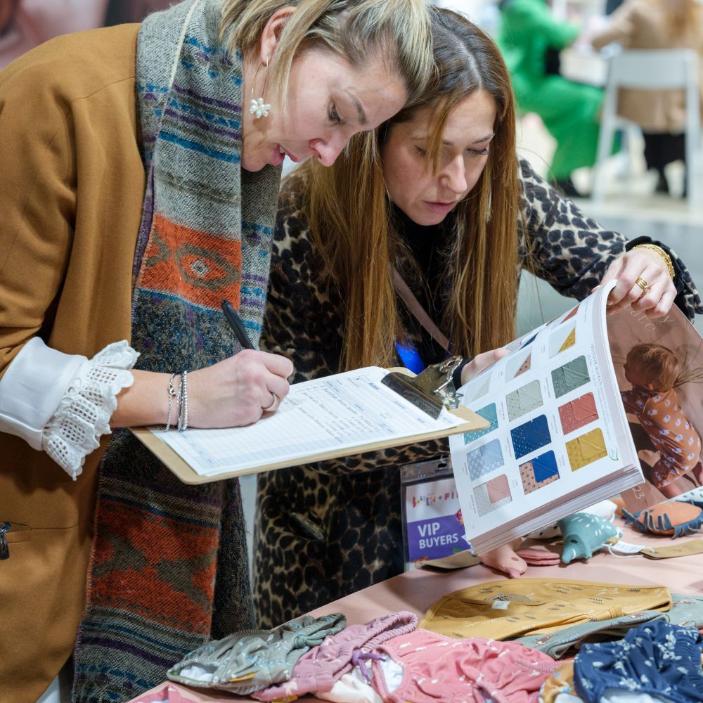 Two woman looking at children's clothes and a catalogue at the Babykid + FIMI trade show 