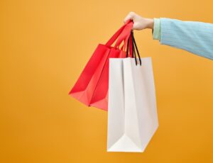An arm holding out shopping bags against a yellow background