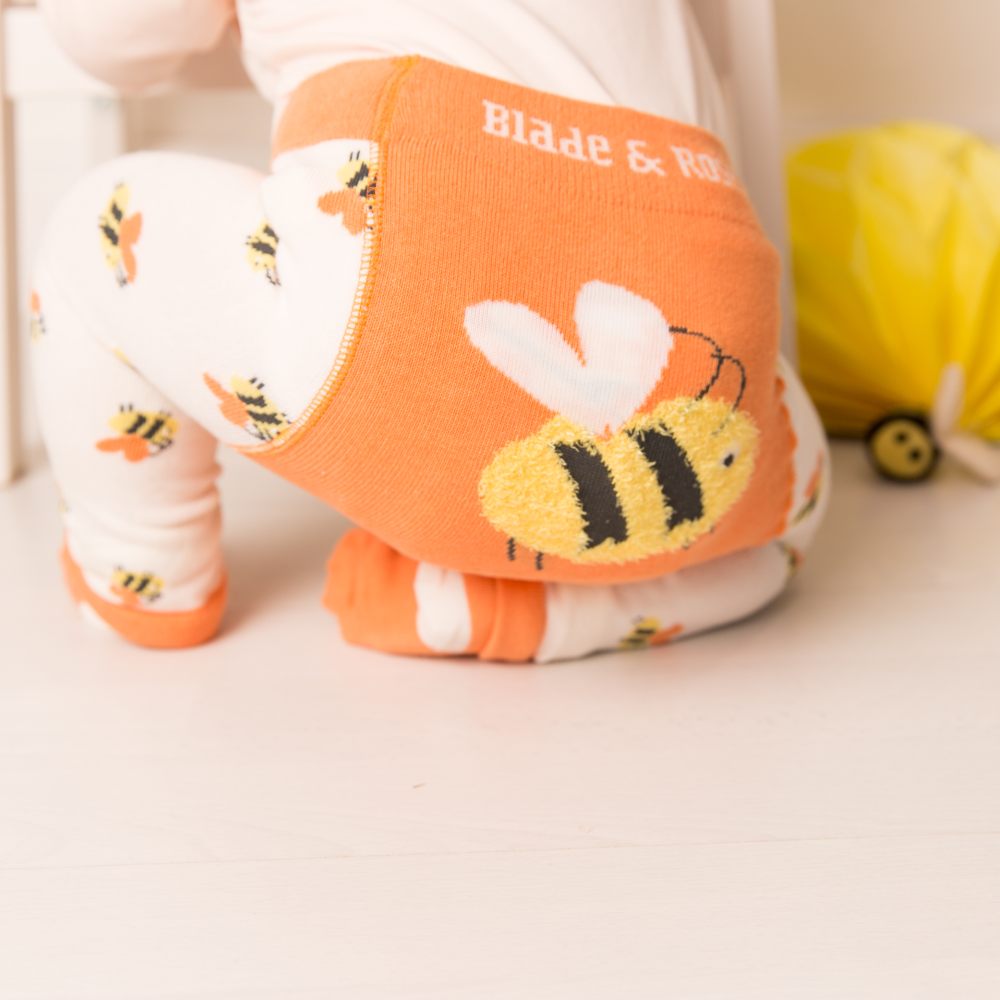 A baby wearing orange leggings with a bumble bee on the bottom